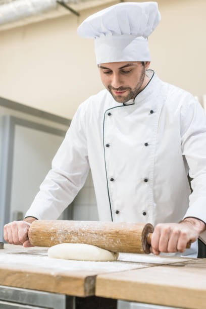 istock Handsome baker rolling out dough on wooden table 1072630564
