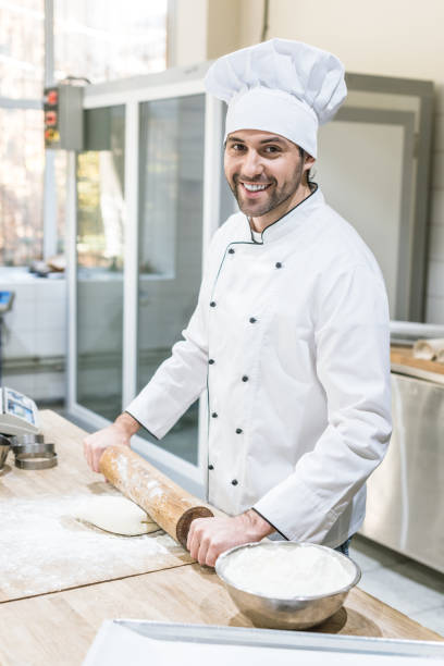 istock Handsome chef smiling and rolling out dough in professional kitchen 1072630592