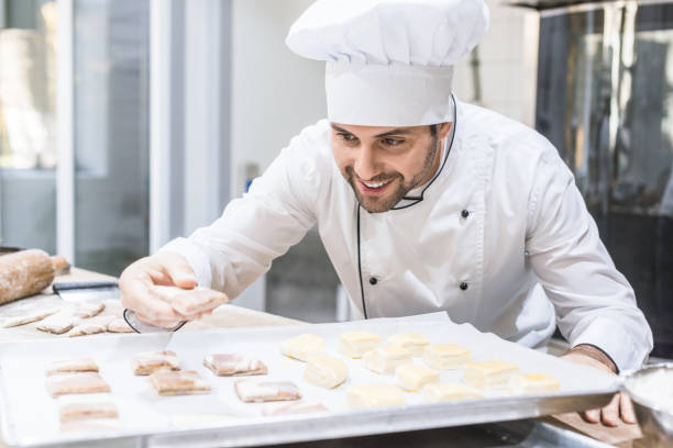 istock Baker in chefs uniform smiling and laying uncooked dough on tray 1072630664