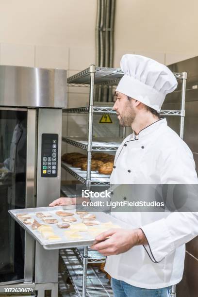 Erwachsenen Bäcker In Weißen Köche Uniform Backblech Mit Rohen Teig Im Ofen Setzen Stockfoto und mehr Bilder von Ausrüstung und Geräte