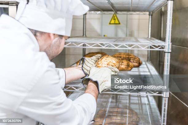 Männliche Bäcker In Weißen Köche Uniform Frisches Warmes Brot In Rack Stockfoto und mehr Bilder von Backen