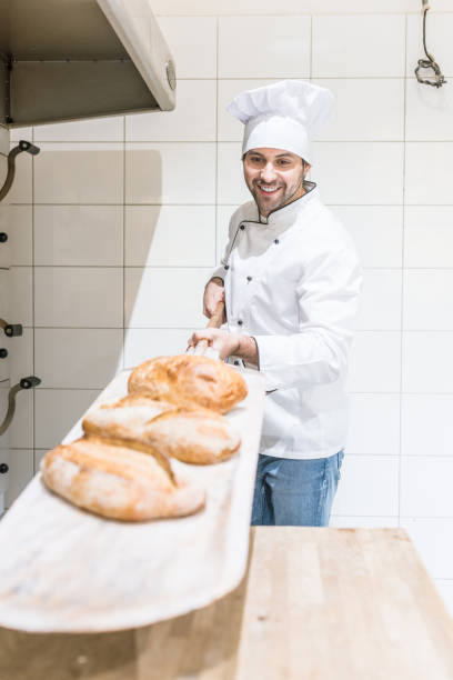 istock Baker holding metal spade with fresh pastry in bakehouse kitchen 1072635506
