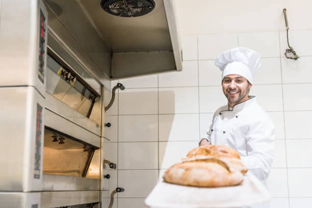 istock smiling baker in white chefs hat holding board with hot fresh bread 1072635510