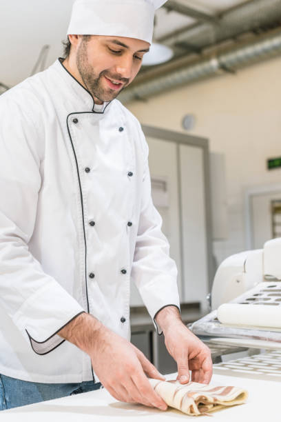 istock Baker in white chefs uniform kneading dough on bakehouse table 1072635552