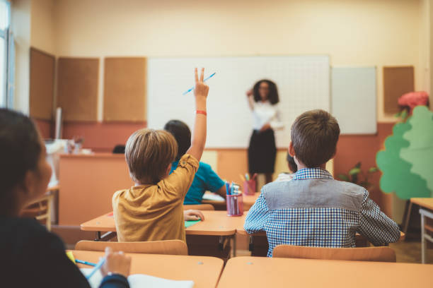 istock Schoolboy with hand raised wants to answer teacher's question in class 1072641088
