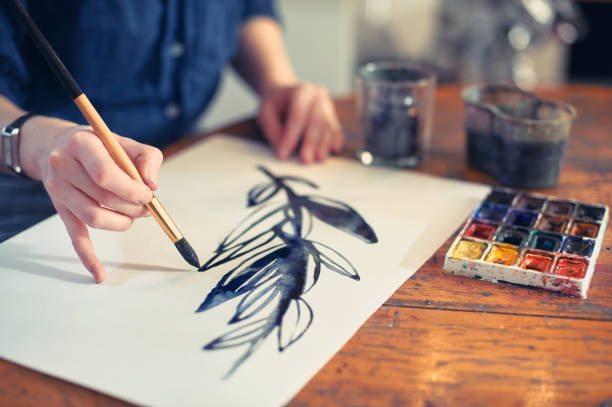 Young Woman Artist Working On Painting In Studio. Selective focus on foreground. Young Woman Artist Working On Painting In Studio. Selective focus on foreground watercolor paints photos stock pictures, royalty-free photos & images