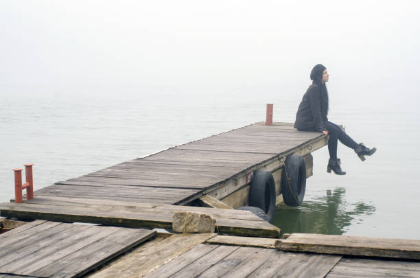 istock Young sad woman sitting on the river dock 1072651416