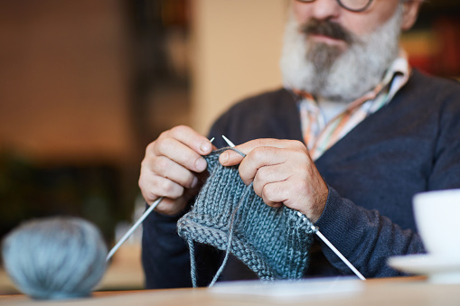 Bearded grandpa knitting warm woolen sweater or other knitwear at lesiure