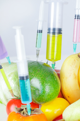 Scientist injecting liquid from syringe into fruits and vegetables. Genetically modified organism - apple and laboratory glassware.