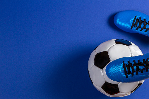 Soccer ball under soccer players feet on blue background.