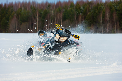 In snowdrift rider loss control and fall off from snowmobile. Reducing risk of injury by safety gear during backcountry tour accident. Extreme sport adventure, outdoor activity during winter holiday.