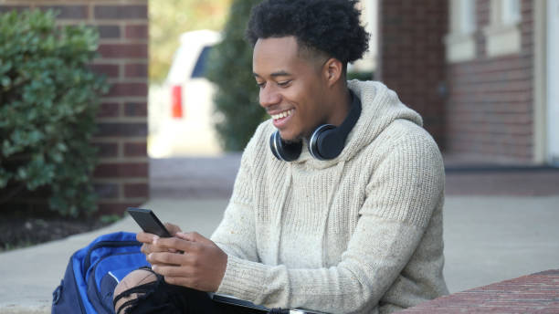 istock Young, college student looks down at his phone, while sitting outdoors 1072675772