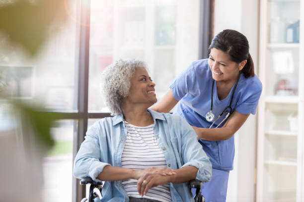 infermiera spinge paziente donna in sedia a rotelle - geriatric nurse foto e immagini stock