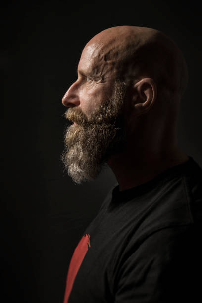 istock a bearded man with a bald head side view and dark background 1072696114