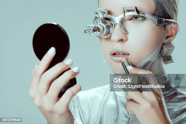 Silver Robot Looking At Mirror And Applying Lipstick Isolated On Grey Future Technology Concept Stock Photo - Download Image Now