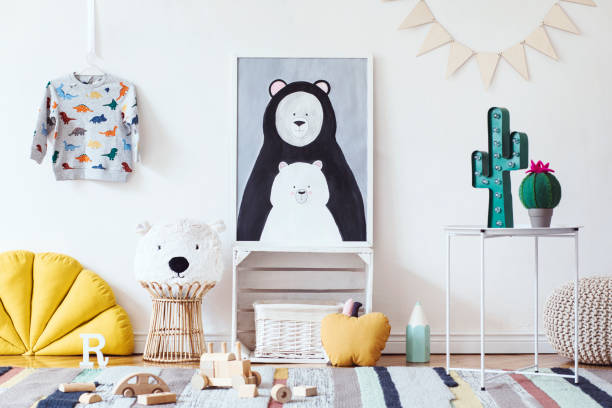 istock Stylish scandinavian kid room with mock up photo poster frame on the pattern wall, boxes, teddy bear and toys. Cute modern interior of playroom with white walls, wooden accessories and colorful toys. 1072749140