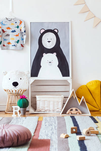 istock Stylish scandinavian kid room with mock up photo poster frame on the pattern wall, boxes, teddy bear and toys. Cute modern interior of playroom with white walls, wooden accessories and colorful toys. 1072749184