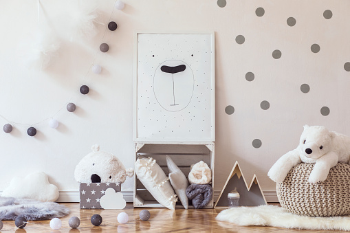 Stylish scandinavian child room with mock up photo poster frame on the pattern wall, boxes, teddy bear and toys.Cute modern interior of playroom with white walls, wooden accessories and colorful toys.
