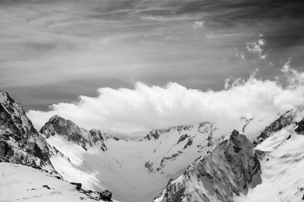 istock Black and white view on snowy sunlight mountains in clouds 1072754842