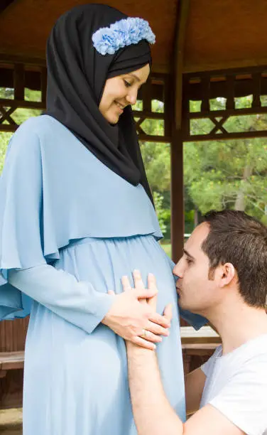 Future dad kissing pregnant wife's belly at the public park. Pregnancy concept.