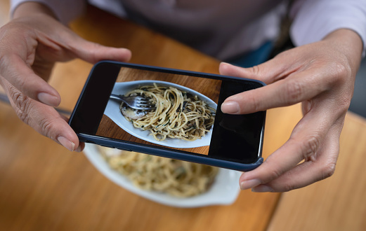Close-up on a woman taking a picture of her food at a restaurant using a cell phone â lifestyle concepts