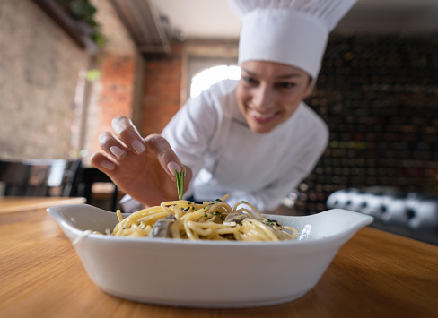 Portrait of a female chef decorating a plate of food at a restaurant while looking very happy - commercial kitchen concepts