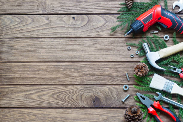 istock Merry Christmas and Happy new year handy construction tools background concept. Hammer, wrenches, screwdriver, pliers, paint brush, pine leaves, pine cones decoration on  wood background. Top view with copy space. 1072840798