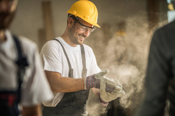 buon operaio che pulisce i guanti dalla segatura in cantiere. - carpenter home addition manual worker construction foto e immagini stock