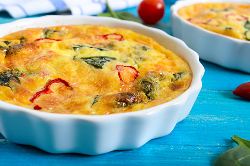 Frittata with fresh vegetables and spinach. Italian omelet in ceramic forms on a blue wooden background.