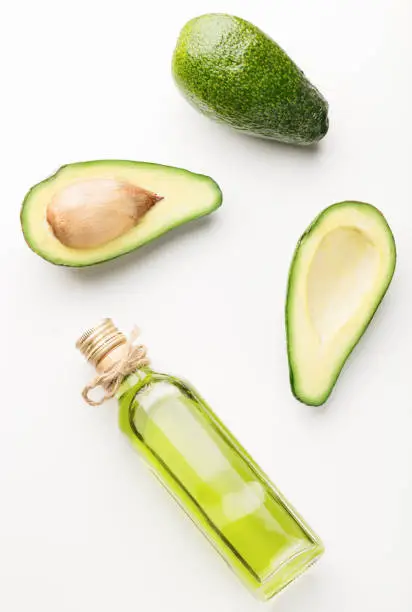 Glass bottle natural avocado oil, three fresh avocados on a white table. Top view