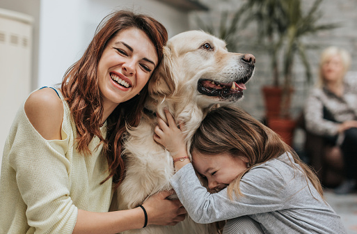 Happy mother and daughter showing affection towards their dog at home.