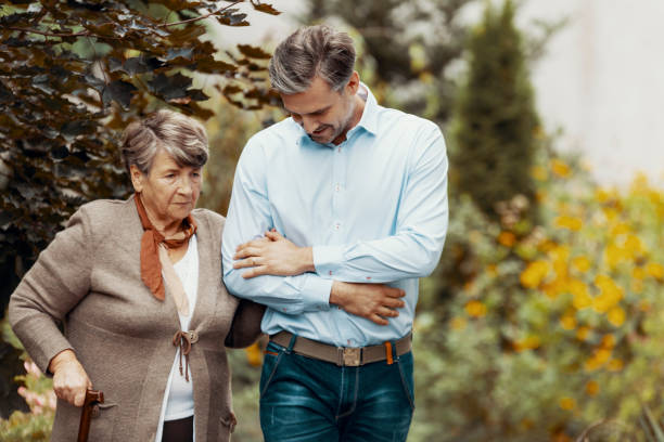 preoccupata donna anziana grigia con bastone da passeggio in giardino con suo figlio - senior male immagine foto e immagini stock