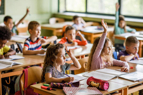 istock Large group of elementary students raising arms in the classroom. 1072959132