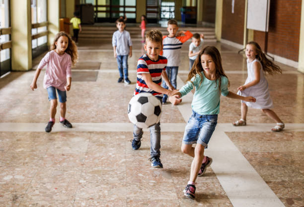 istock Playful school kids having fun while playing with ball in a hallway. 1072964934