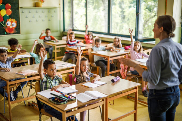 istock School kids raising their arms during teacher's lesson at elementary school. 1072969864