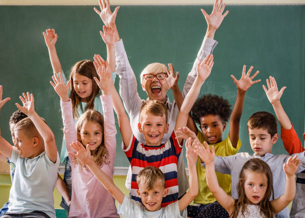 istock Happy teacher and elementary students with raised arms in the classroom. 1072970028