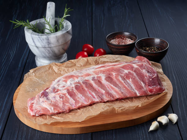 Raw pork ribs on crumpled paper on a bamboo cutting board Raw pork ribs on crumpled paper on a bamboo cutting board, with rosemary twigs, tomatoes, garlic cloves, peppercorns and coarse pink salt pink pepper spice ingredient stock pictures, royalty-free photos & images
