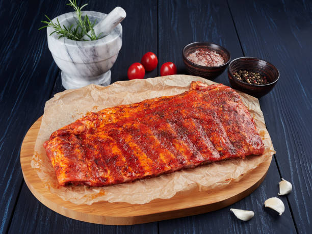 Marinated raw pork spare ribs on crumpled paper on a bamboo cutting board Marinated raw pork spare ribs on crumpled paper on a bamboo cutting board, with rosemary twigs, tomatoes, garlic cloves, pepper corns and coarse pink salt pink pepper spice ingredient stock pictures, royalty-free photos & images