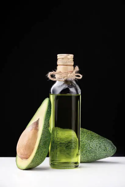 Natural avocado oil for cooking. Two fresh tropical fruit avocado, cut on a white table. on a black background