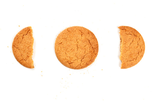 A photo of a single ginger cookie with two halves, shot from the top on a white background with crumbs and a place for text