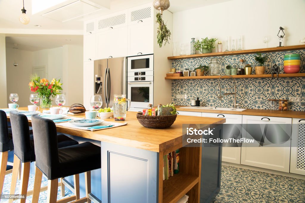 Fresh summer breakfast in Mediterranean style kitchen. Bright and sunny space with a lot of herbs and plants. Modern kitchen with open space. Modern composition of breakfast table in mediterranean's kitchen. Kitchen Stock Photo
