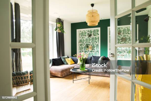 Stylish Interior With Sofa Colors Pillows Flowers And Wooden Floor Sunny And Bright Living Room With Big Window And Design Commode Stock Photo - Download Image Now