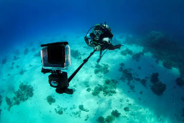 Male scuba diver using an action camera on a selfie stick to take some underwater shots.