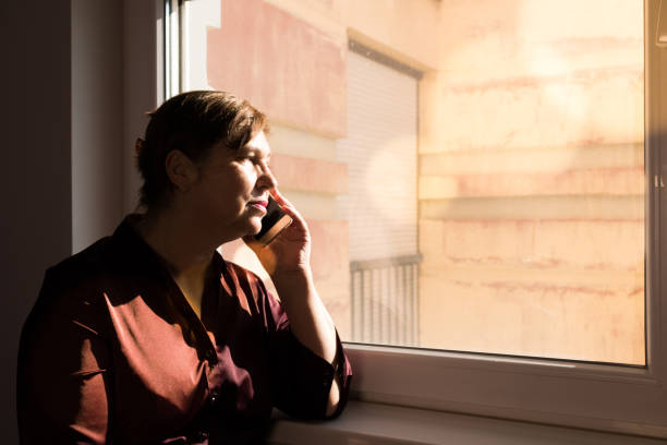 istock Thoughtful mature woman talking on mobile phone by the window. 1073005538