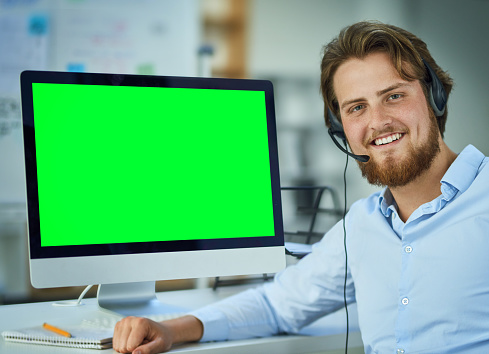 Portrait of a call centre agent sitting at a computer with a green screen in an office