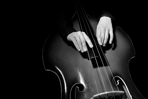 Two hands playing gently on double bass on dark background