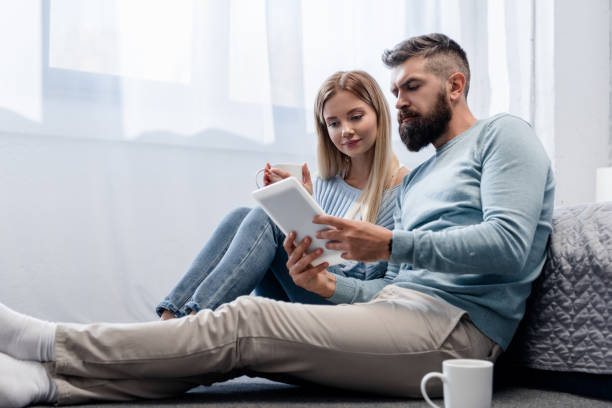 istock Couple sitting on floor with digital tablet and drinks 1073021884