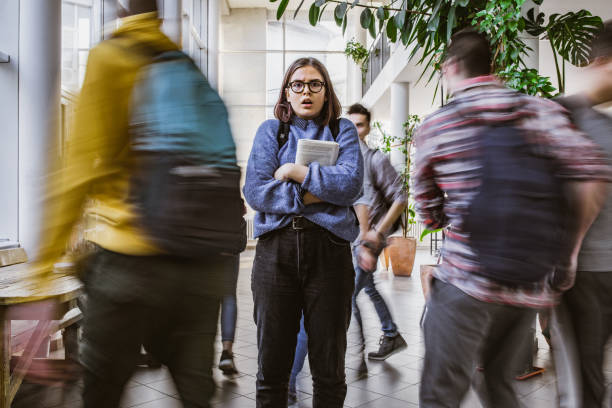 Shocked nerdy student among her classmate in blurred motion. Fearful female student looking at camera while other students are walking around her in blurred motion. nerd teenager stock pictures, royalty-free photos & images