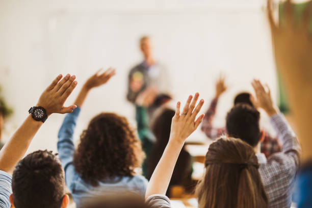 Back view of students raising hands on a class. Rear view of large group of students raising their hands to answer the question on a class. q and a stock pictures, royalty-free photos & images