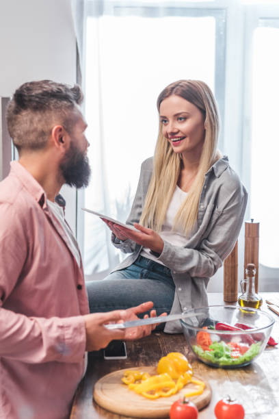istock Husband preparing salad and wife sitting on table with digital tablet 1073045636